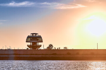 Silhouette of tourist observation spherical tower in the rays of the sun on the coast of China. View from a pleasure boat from the border river Amur. Border between Russia and China