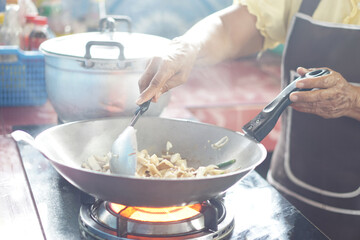 Close up woman is cooking, stirring food in a frying pan on stove by using ladle. Motion shot.  Concept, cooking method. Kitchen time. Household daily routine. Preparing breakfast, lunch or dinner. 