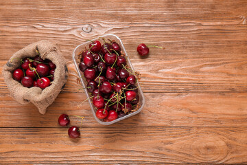 Plastic container and basket with fresh cherry on wooden background