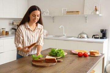 Young woman making tasty sandwich in kitchen