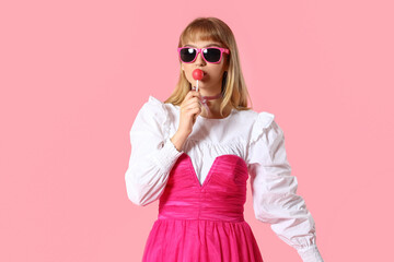 Young woman in doll clothes with lollipop on pink background