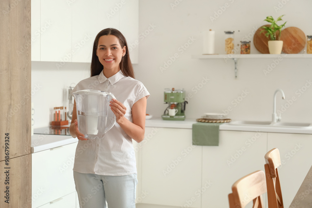 Poster beautiful young woman with water filter jug in kitchen