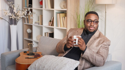 Morning coffee. Home relaxing. Cozy leisure. Pleased dreamy man drinking mug of hot tea enjoying Sunday weekend rest on couch in living room copy space.