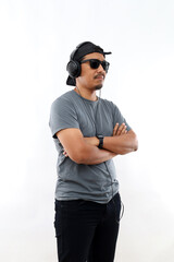 Fototapeta premium Asian man enjoying his favorite music. Happy stylish man in black hat and sunglasses with headphones listening and smiling while standing against white background