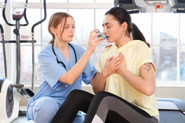 Female doctor with inhaler giving young woman first aid in gym
