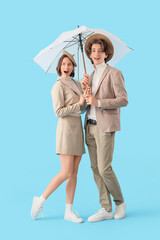 Stylish young couple with umbrella on blue background