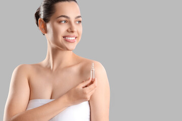 Beautiful young woman holding ampule on grey background