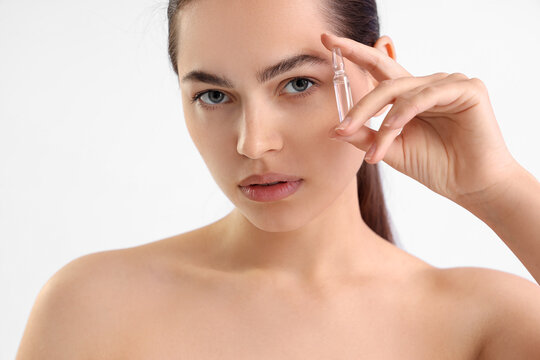 Beautiful young woman holding ampule on white background