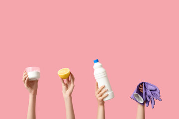 Female hands holding bottle of detergent, lemon, jar with cleaning agent and rubber gloves on pink background