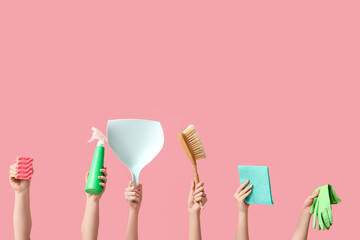 Female hands holding bottle of detergent, rag, rubber gloves, dustpan, broom and sponge on pink background