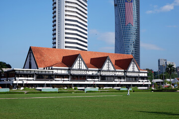 a large green park with a scenic view of vintage buildings and the Malaysian flag on a bright sunny day, clear blue sky, Dataran Merdeka or Merdeka Square area in KL city, green environment