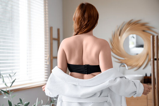 Beautiful plus size woman with bathrobe in bathroom, back view