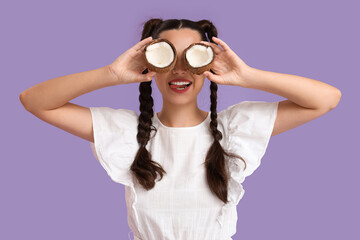 Beautiful young happy woman with braids holding halves of fresh coconut on purple background