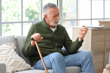 Senior man suffering from Parkinson syndrome with stick on sofa at home