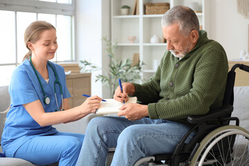 Senior man suffering from Parkinson syndrome in wheelchair with nurse drawing on notebook at home