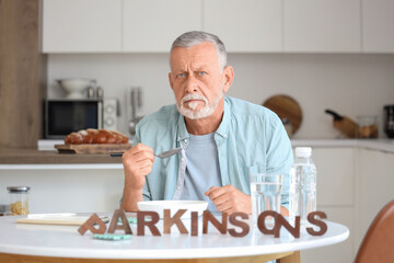 Senior man suffering from Parkinson syndrome eating at table in kitchen