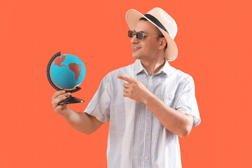 Male tourist pointing at globe on orange background