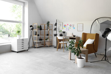 Photographer workplace with armchair, laptop and lighting equipment in modern photo studio