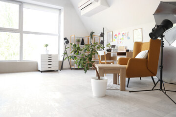 Photographer workplace with armchair, laptop and lighting equipment in modern photo studio