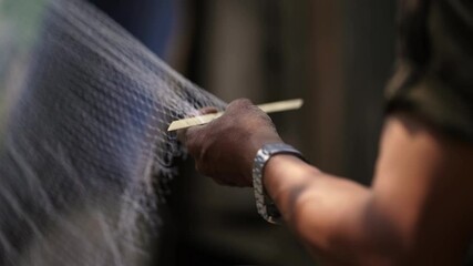 Close-up view of a man weaving a traditional fishing net by hand, using techniques from an Asian village in a Nepali rural setting