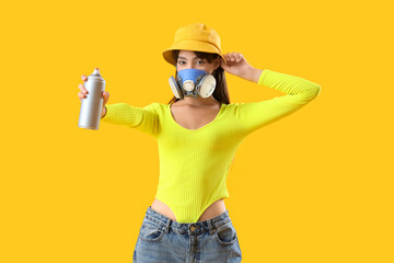 Young girl in respirator and with spray can on yellow background