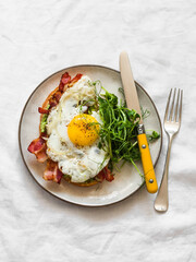 Sandwich with avocado, bacon, fried egg and pea sprouts on a light background, top view