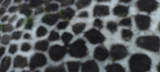 Stone wall texture blur background - bokeh background of black stone siding with round shaped stones