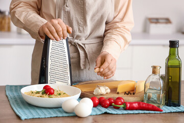 Woman grating garlic at table in kitchen, closeup