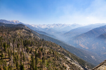View of the Sierra Nevada mountain range from Moro Rock Trail in Sequoia National Park, California, showcasing forested slopes and distant peaks under a clear blue sky.