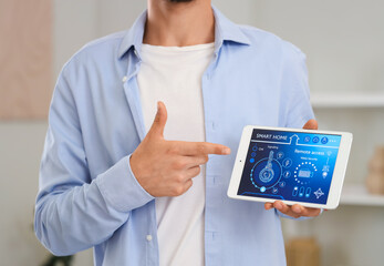 Young man pointing at smart home control panel in room