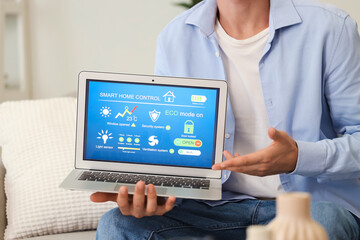 Young man holding laptop with smart home application in room, closeup