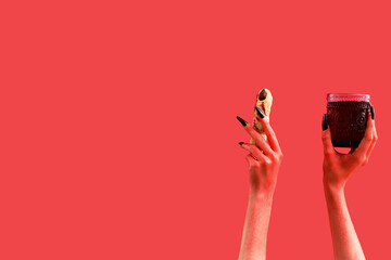 Devil hands with glass of blood and cookie in shape of finger on red background. Halloween celebration