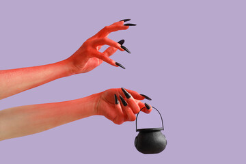 Devil hands with cauldron on lilac background. Halloween celebration