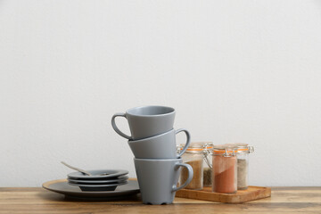 Cups, saucers and spices on wooden table near white wall