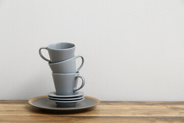 Stack of cups and saucers on wooden table near white wall