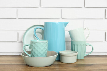 Cups, bowls and jug on wooden table near white brick wall