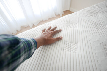 Hand touching and pressing orthopedic mattress on bed.