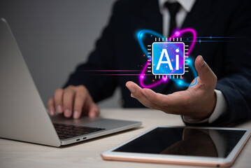 Businessman presenting a glowing AI icon above his hand, with a laptop and tablet on the desk, representing artificial intelligence technology.