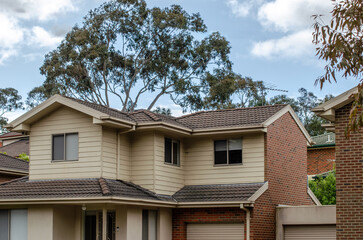 A two-story Australian suburban house with a beige facade and a brown tiled roof in a neighborhood. Concept of homes, real estate investment, property or dwelling.
