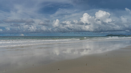Beautiful seascape. The waves of the turquoise ocean are foaming, spreading over the sandy beach. Picturesque clouds in the blue sky. Reflection on the wet smooth sand. Malaysia. Borneo. Kota Kinabalu