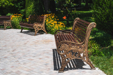 Beautiful wooden decorative benches in the city park against the background of trees.