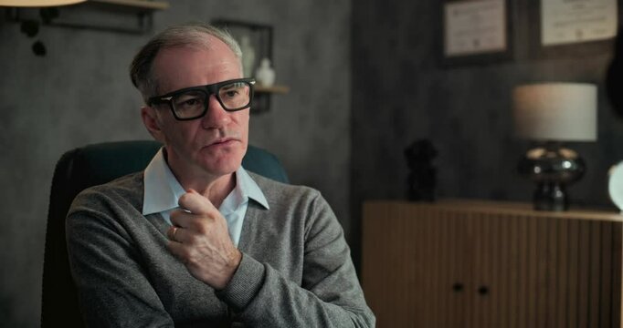 Senior psychotherapist in glasses sits in chair, listens to patient and asks questions during psychological rehabilitation. Professional military psychologist conducts therapy session. Mental health.