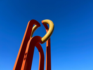 Abstract sculpture against a vibrant blue sky ; A playful interplay of shapes and colors ; Modern art stands tall under a clear sky