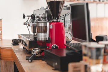 A cozy coffee shop counter featuring a red grinder, espresso machine, and computer, creating a vibrant coffee brewing atmosphere.