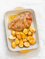 Cooking lunch - raw pickled chicken breast and baby potatoes in a baking dish on a light background, top view