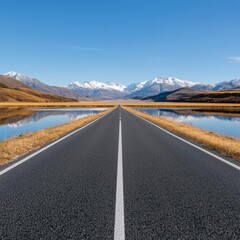 Fototapeta premium Scenic road leading towards snow-capped mountains with blue sky and clear reflections.