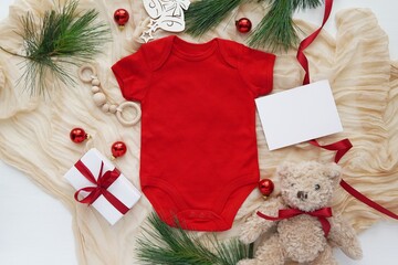 Christmas baby or pregnancy announcement template, red baby bodysuit mockup, empty card, Christmas decorations, gift, creative flat lay composition.
