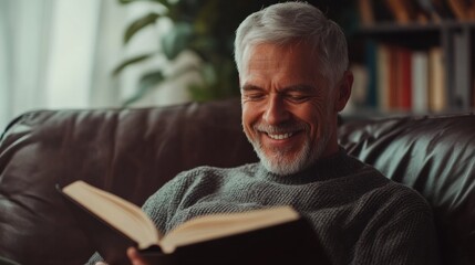 Grey-haired man smiling while reading a book at home, enjoying a quiet and peaceful afternoon in his cozy living room.