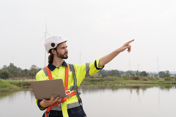 Male engineer working with laptop computer for maintenance of wind turbines at windmill field farm. Male engineer repairing or maintaining wind turbines at wind turbines farm