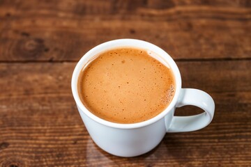 Fototapeta premium A white ceramic cup of coffee placed on a wooden surface, suitable for designs involving relaxation, cafes, or morning themes.